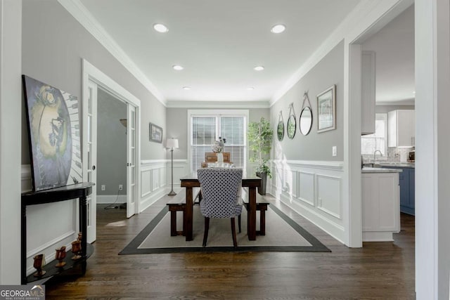 dining space featuring dark wood finished floors, crown molding, a decorative wall, and a wainscoted wall