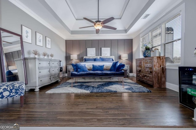 bedroom with a tray ceiling, visible vents, baseboards, and wood finished floors