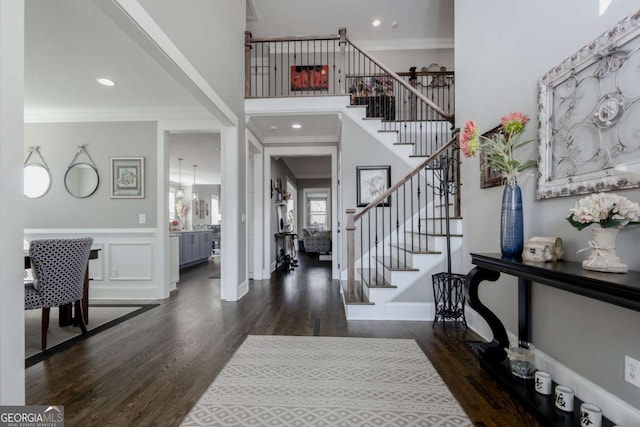 entryway featuring stairway, wood finished floors, a wainscoted wall, a towering ceiling, and crown molding