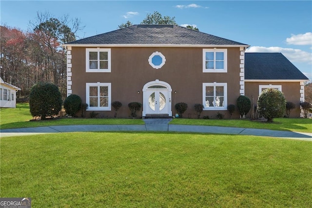 colonial-style house featuring a shingled roof, a front yard, and stucco siding