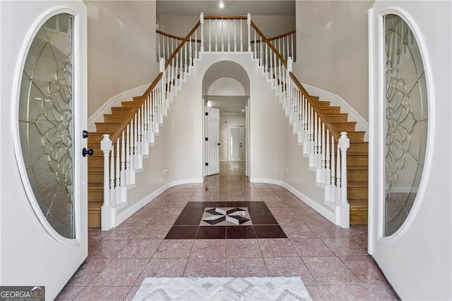 entryway featuring stairs, baseboards, arched walkways, and a towering ceiling