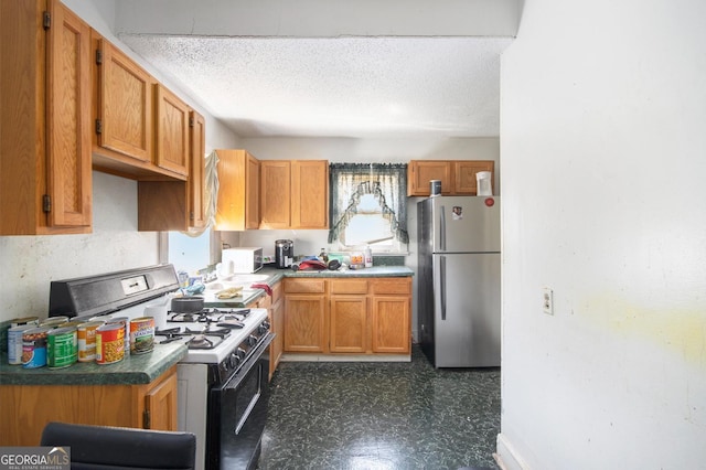 kitchen featuring brown cabinets, range with gas stovetop, a textured ceiling, freestanding refrigerator, and dark floors