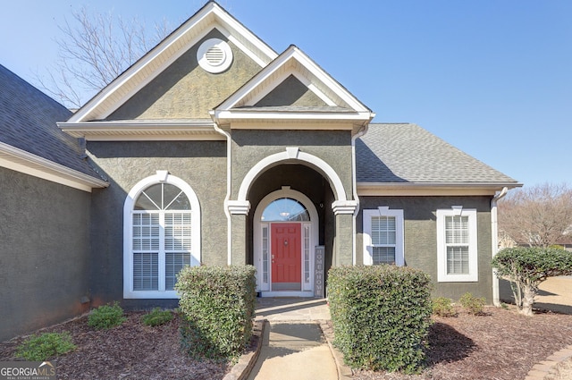 view of exterior entry with roof with shingles and stucco siding