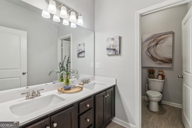 bathroom with double vanity, toilet, baseboards, and a sink