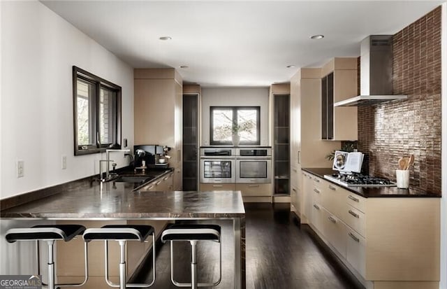 kitchen with a sink, dark countertops, appliances with stainless steel finishes, and wall chimney exhaust hood