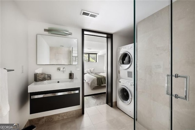 clothes washing area featuring light tile patterned floors, stacked washer / drying machine, visible vents, and laundry area