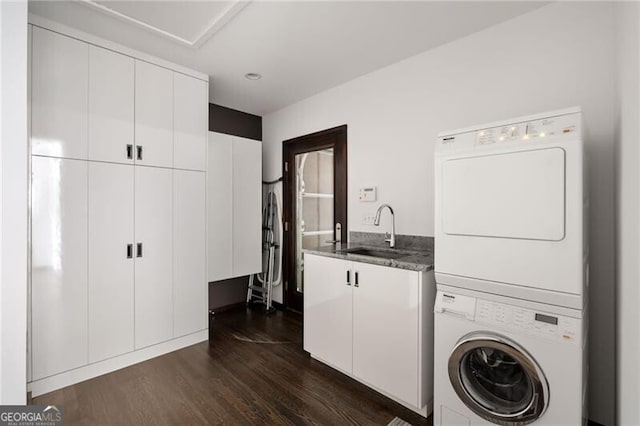 washroom featuring a sink, cabinet space, dark wood-type flooring, and stacked washing maching and dryer