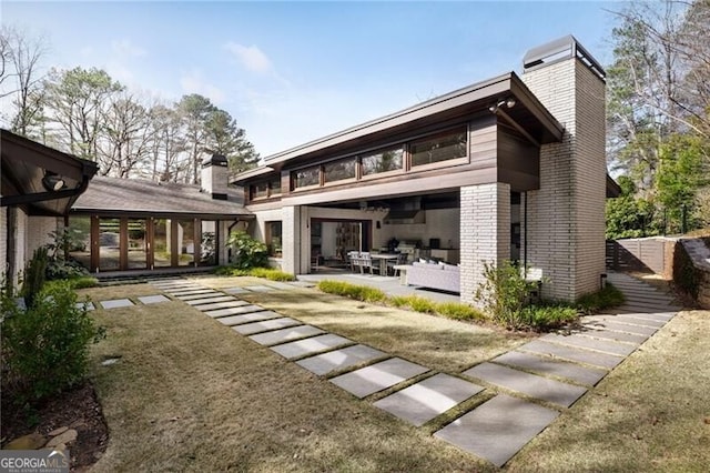 back of property featuring a patio area, a chimney, and brick siding