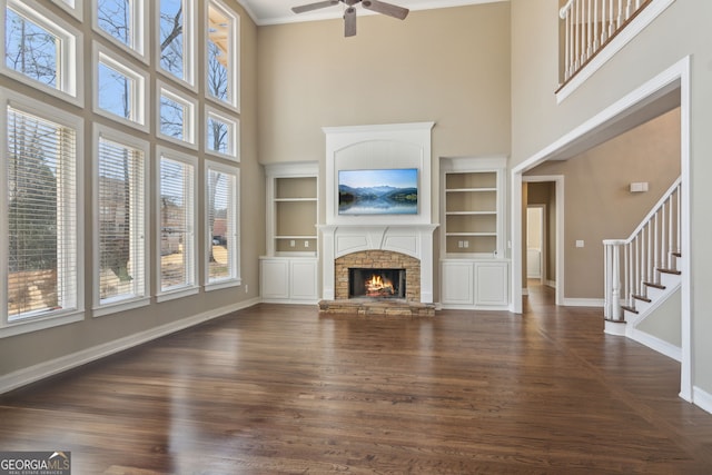 unfurnished living room featuring built in shelves, a ceiling fan, baseboards, a fireplace, and dark wood-style flooring