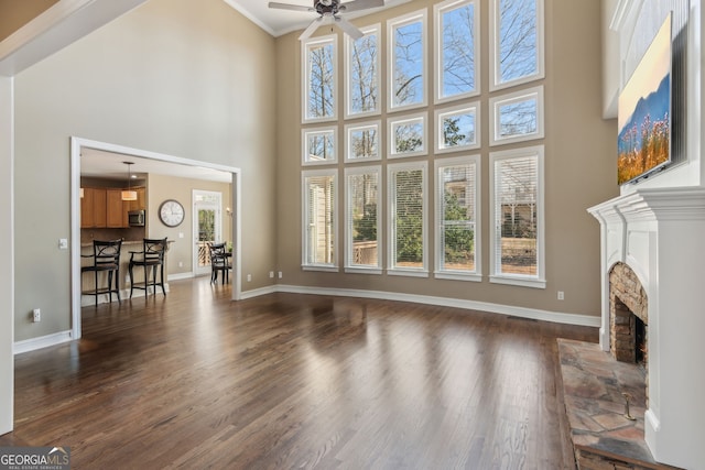 living area with baseboards, dark wood finished floors, a fireplace, ceiling fan, and crown molding