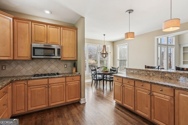 kitchen with tasteful backsplash, dark wood-type flooring, pendant lighting, dark stone counters, and stainless steel appliances