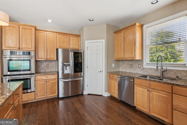 kitchen featuring a sink, stone countertops, dark wood finished floors, stainless steel appliances, and decorative backsplash