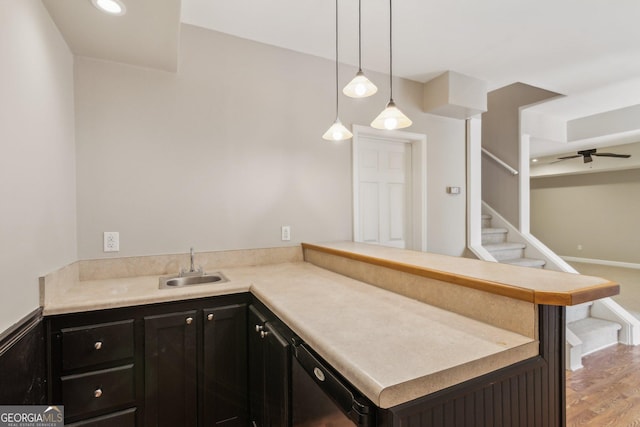 kitchen with a sink, pendant lighting, a peninsula, light wood-style floors, and dark cabinets