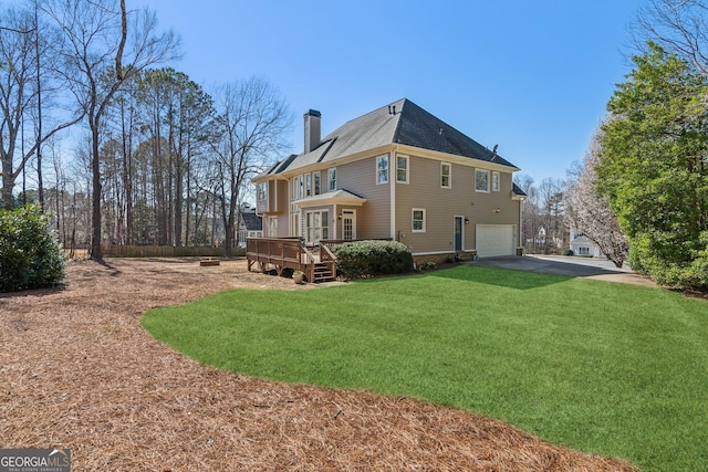 back of house with driveway, a wooden deck, a yard, a chimney, and a garage