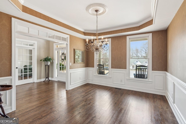 unfurnished dining area with a wainscoted wall, dark wood-type flooring, a healthy amount of sunlight, and a chandelier