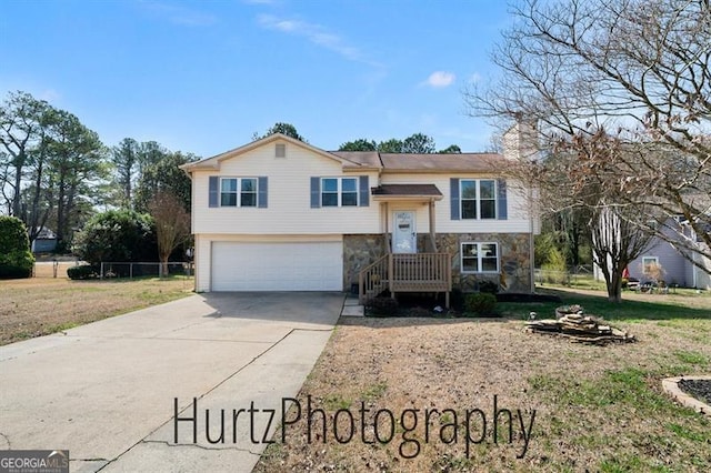 split foyer home with a garage, stone siding, a chimney, and driveway