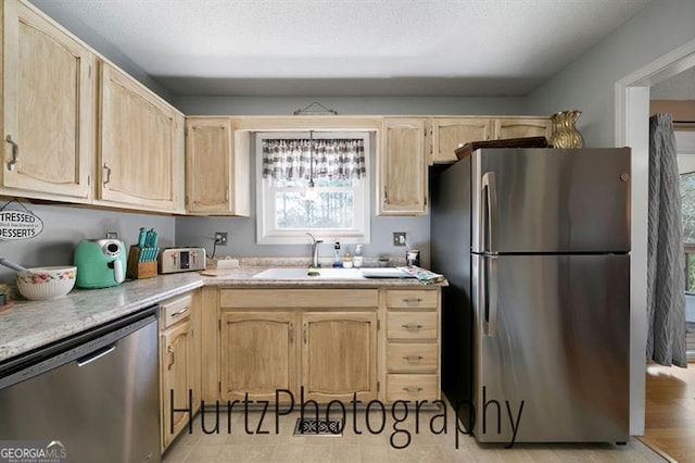 kitchen with light brown cabinets, a sink, stainless steel appliances, light countertops, and a textured ceiling