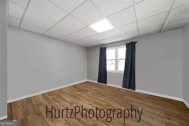 unfurnished room featuring a drop ceiling, baseboards, and wood finished floors