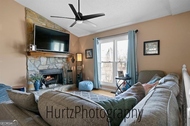 living room featuring a textured ceiling, ceiling fan, a fireplace, and vaulted ceiling