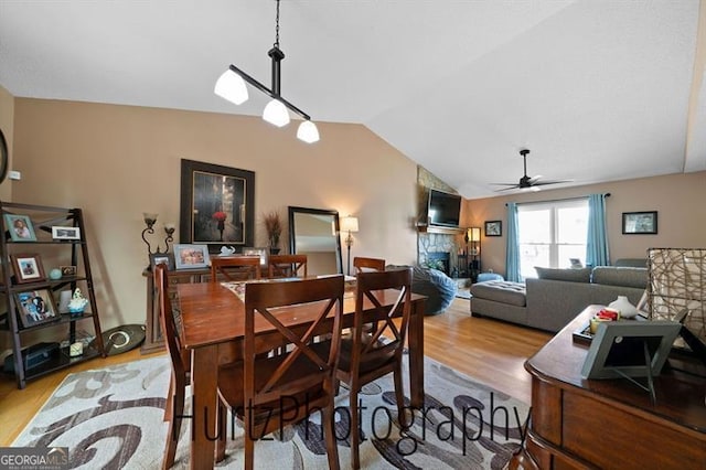 dining space featuring a fireplace, wood finished floors, ceiling fan, and vaulted ceiling