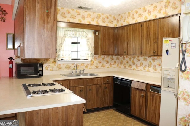 kitchen with wallpapered walls, a sink, black appliances, light countertops, and a textured ceiling