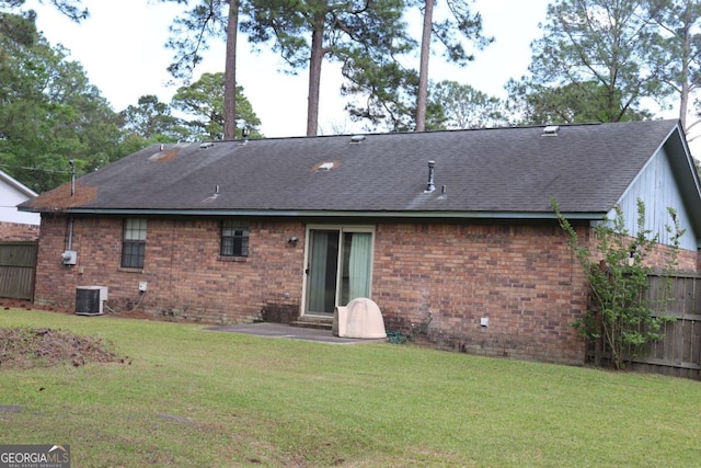 rear view of house with a yard, brick siding, roof with shingles, and fence