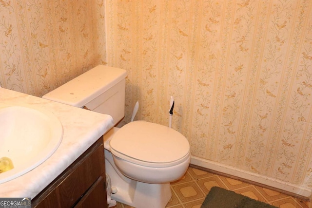 bathroom featuring toilet, vanity, and wallpapered walls