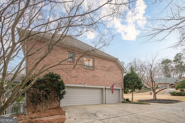 view of side of property featuring brick siding, concrete driveway, and an attached garage