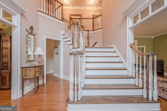 staircase with baseboards, wood finished floors, a high ceiling, and ornamental molding