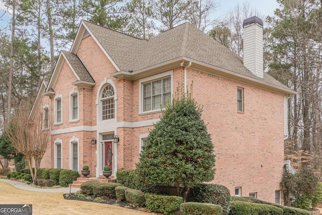 view of side of property featuring brick siding, a chimney, and a shingled roof
