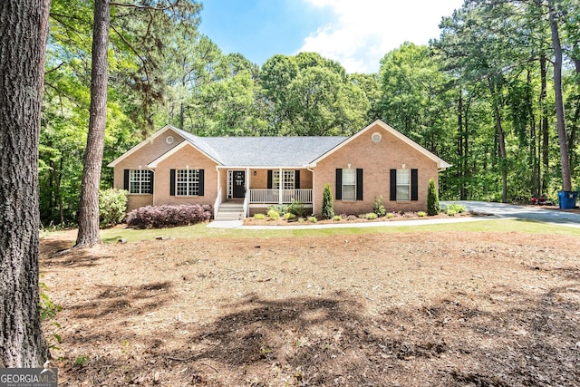 single story home with brick siding, a porch, and a forest view