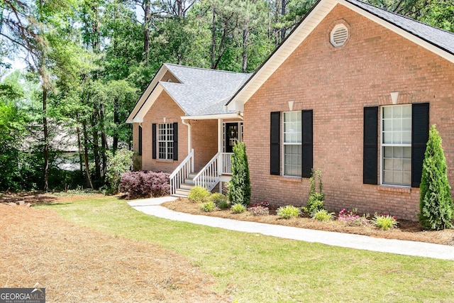 view of front of property featuring brick siding, a shingled roof, and a front lawn