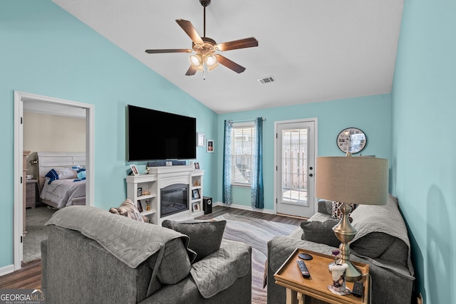 living area featuring visible vents, vaulted ceiling, wood finished floors, a glass covered fireplace, and a ceiling fan