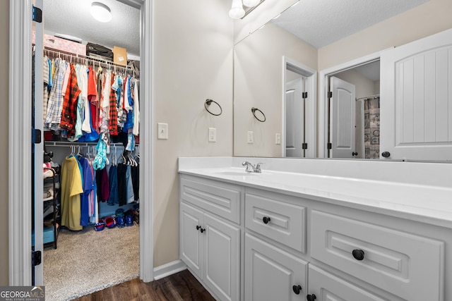 full bathroom featuring vanity, a walk in closet, and a textured ceiling