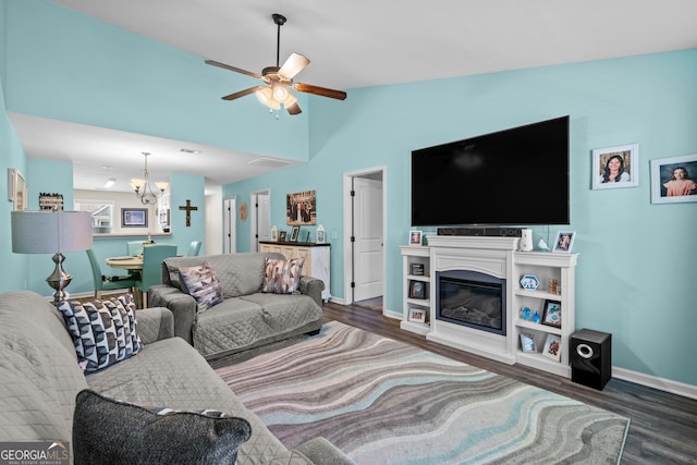 living area with ceiling fan with notable chandelier, vaulted ceiling, wood finished floors, and baseboards