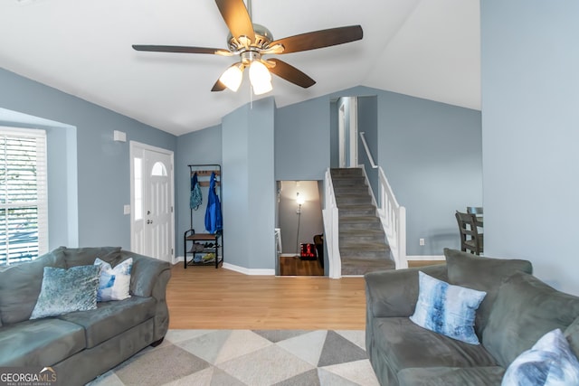 living room featuring wood finished floors, baseboards, a ceiling fan, lofted ceiling, and stairs