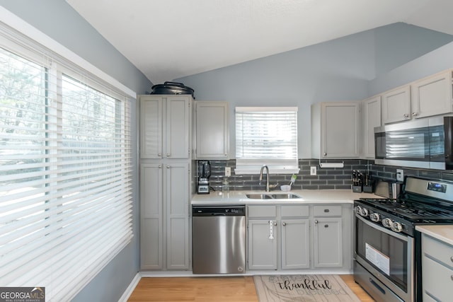 kitchen with a sink, lofted ceiling, appliances with stainless steel finishes, and light countertops