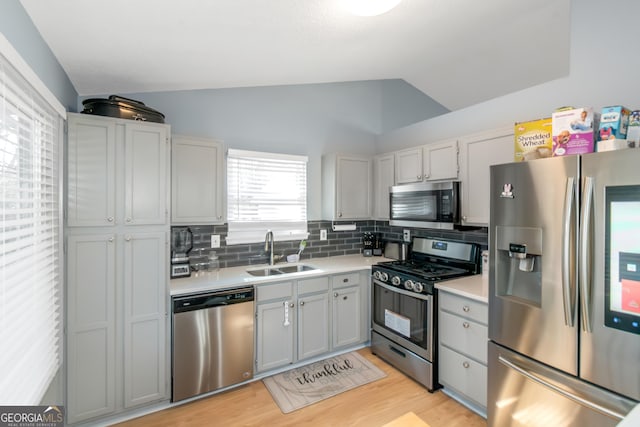 kitchen with lofted ceiling, a sink, light countertops, appliances with stainless steel finishes, and tasteful backsplash