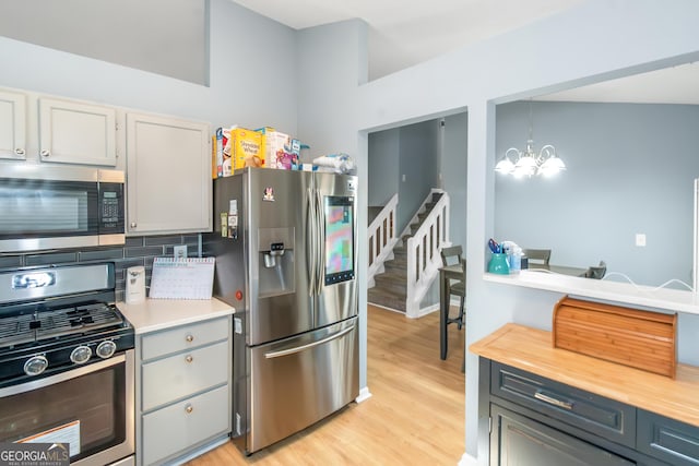 kitchen with an inviting chandelier, light wood-style flooring, decorative backsplash, appliances with stainless steel finishes, and decorative light fixtures