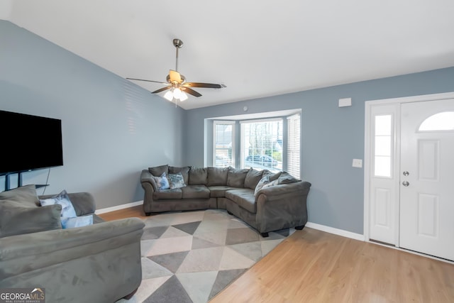 living room featuring light wood-style flooring, a ceiling fan, lofted ceiling, and baseboards