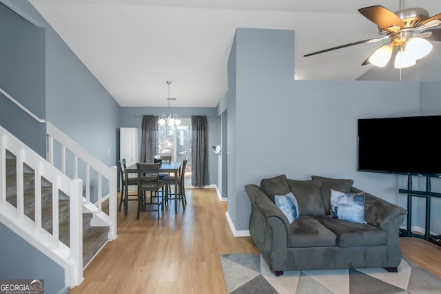 living area featuring ceiling fan with notable chandelier, stairway, light wood-style flooring, and baseboards