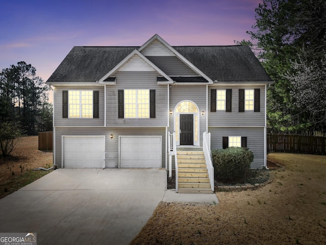 raised ranch with roof with shingles, concrete driveway, an attached garage, and fence