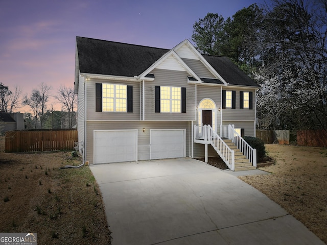 raised ranch featuring an attached garage, concrete driveway, roof with shingles, and fence