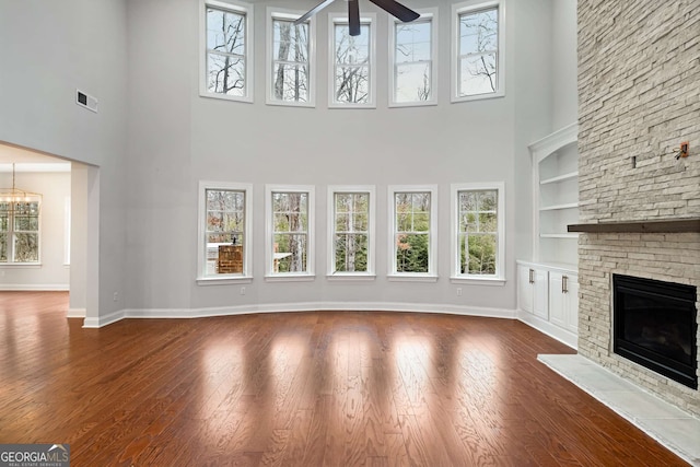 unfurnished living room with built in shelves, visible vents, baseboards, dark wood finished floors, and a stone fireplace