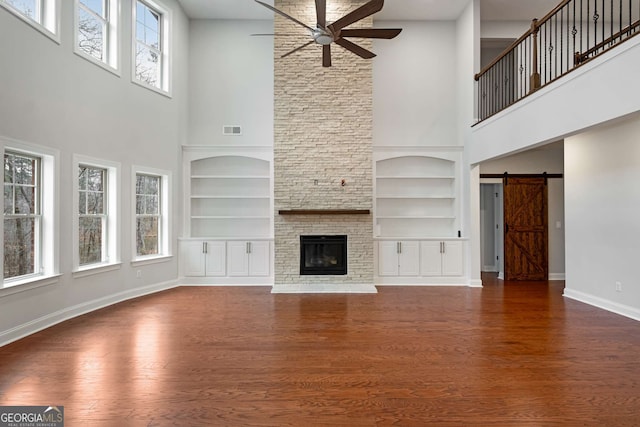 unfurnished living room with visible vents, a ceiling fan, wood finished floors, a barn door, and baseboards