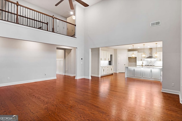 unfurnished living room with visible vents, dark wood-type flooring, a ceiling fan, a sink, and baseboards