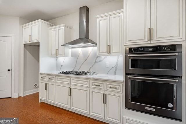 kitchen with dobule oven black, backsplash, wood finished floors, stainless steel gas stovetop, and wall chimney range hood