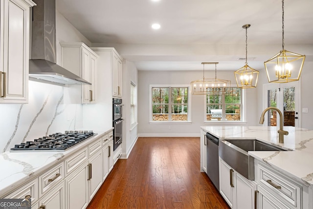 kitchen with a sink, stainless steel appliances, wall chimney exhaust hood, decorative backsplash, and hanging light fixtures