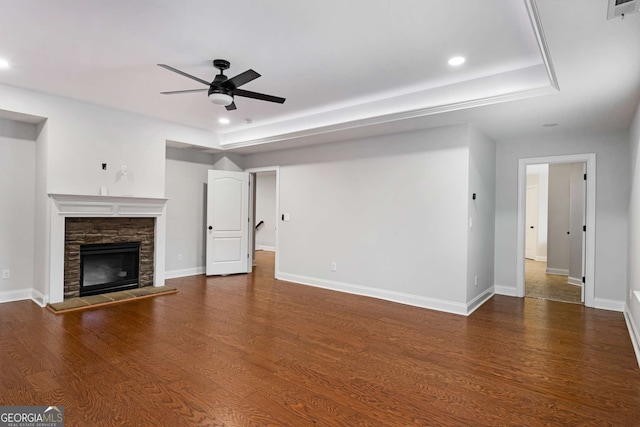 unfurnished living room with wood finished floors, baseboards, a tray ceiling, a fireplace, and ceiling fan