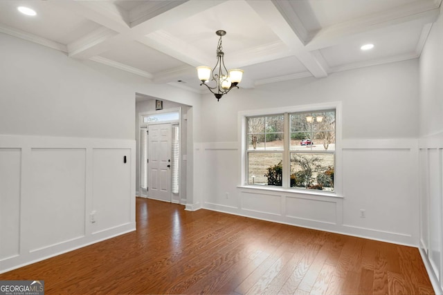 unfurnished dining area featuring beamed ceiling, coffered ceiling, a decorative wall, and wood finished floors